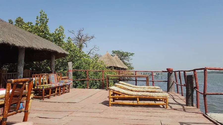 A riverside deck with sun loungers and thatched huts at Bintang Bolong Lodge